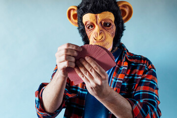 Man wearing monkey mask and holding poker playing cards on blue background.