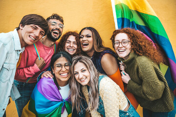 Diverse group of young people celebrating gay pride festival day - Lgbt community concept with guys and girls hugging together outdoors - Multiracial trendy friends standing on a yellow background