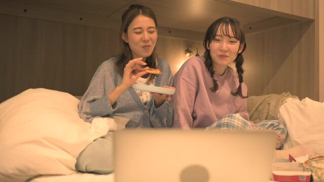 ベッドの上でジャンクフードを食べながら映画を見る女性達