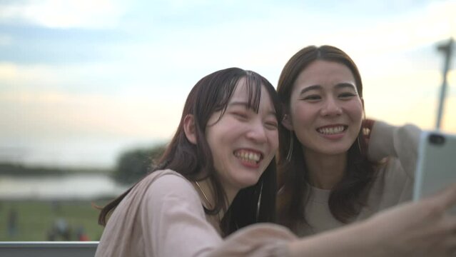 夕暮れの公園でスマートフォンを使ってセルフィーを撮る二人の女性