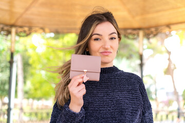 Young pretty Romanian woman holding a wallet at outdoors with sad expression