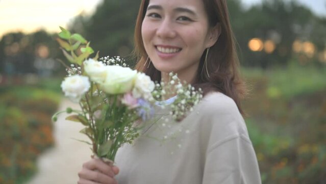 夕方の公園で花束を持って微笑む女性