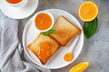 Toasts with orange marmalade or orange jam with cup of tea on a gray background. Delicious breakfast. Copy space.