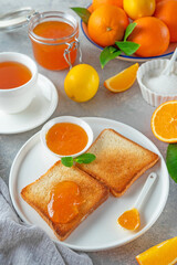 Fototapeta na wymiar Toasts with orange marmalade or orange jam with cup of tea on a gray background. Delicious breakfast. Copy space.