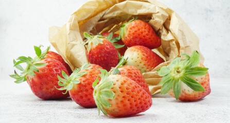 Close up, strawberries on a stone base and inside a kraft paper bag.