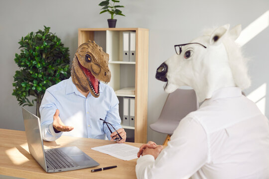 People with funny animal heads at bizarre job interview. Man wearing dinosaur mask sitting at office table with HR manager in horse mask, answering questions and telling about his work experience