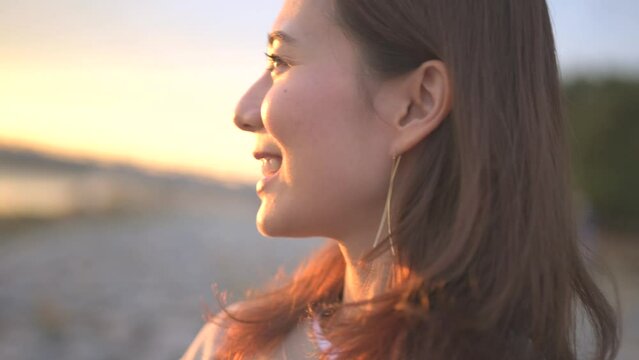 川辺で夕焼けの空を眺める女性の横顔アップ