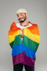 Joyful gay man holding lgbt flag and closing eyes isolated on grey.