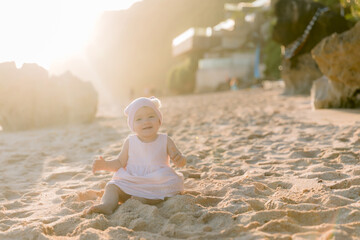 Fototapeta na wymiar Portrait of laughing baby girl in pink dress on sea beach with warm sunlight.