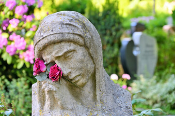 Die Trauernde mit betenden Händen und Blumen vor Gräbern