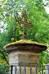 Altes Metallkreuz auf bemooster Säule mit seitlichem Lichtschein