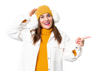 Middle age woman wearing winter muffs over isolated chroma key background surprised and pointing...