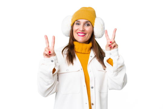 Middle age woman wearing winter muffs over isolated chroma key background showing victory sign with both hands
