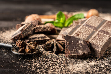 Close-up of chocolate with cocoa powder, hazelnuts, mint and star anise, on dark table, black background, horizontal, with copy space