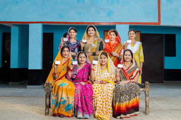 Group of happy traditional indian women wearing sari sitting together showing blank id or business...