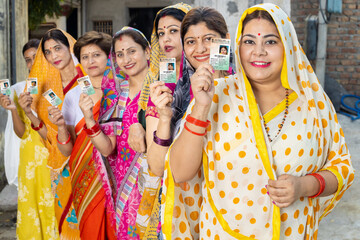 Group of happy traditional indian women standing in queue showing voter card id to cast vote at...