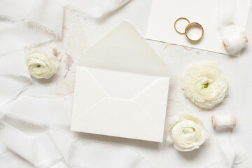 Blank envelope near cream roses, white silk ribbons and wedding rings top view, wedding mockup