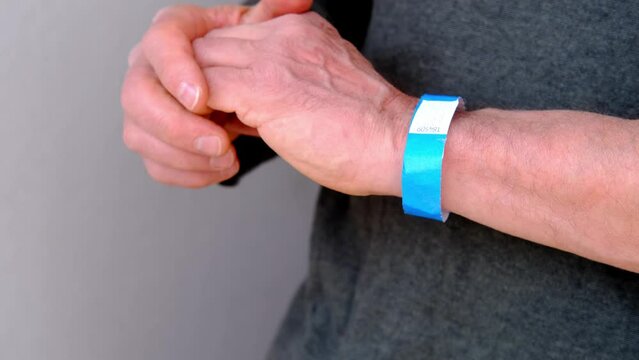 Blank paper wristband mockup on persons arm. Clear adhesive bangle wristlet sticker with entry number on hand of middle-aged european man, blue paper bracelet, check tape, event ticket concept