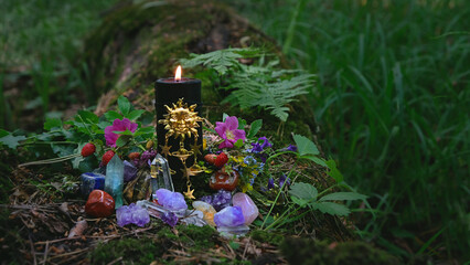 Burning black candle with sun amulet, gemstones, flowers in forest, dark natural abstract background. esoteric ritual for Summer solstice, Midsummer, Litha. pagan witch tradition, wiccan practice - obrazy, fototapety, plakaty
