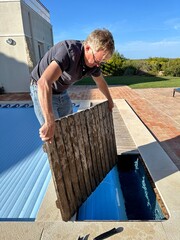 Man replacing the decking which hides the roller for a hidden slatted automatic pool cover