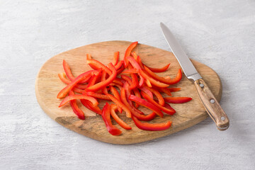 Wooden board with chopped sweet red peppers on a light gray background, top view. Stage of cooking healthy vegan food