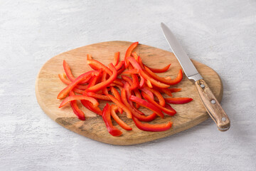Wooden board with chopped sweet red peppers on a light gray background, top view. Stage of cooking...
