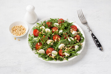 Salad with arugula, cherry tomatoes, mini mozzarella and pine nuts on a light gray background. Delicious homemade traditional food