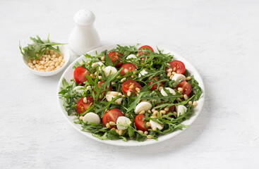 Salad with arugula, cherry tomatoes, mini mozzarella and pine nuts on a light gray background. Delicious homemade traditional food