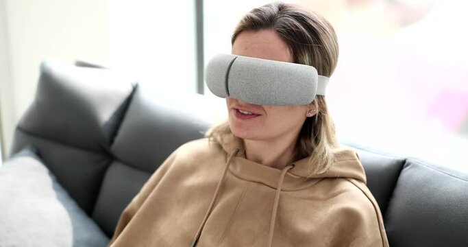 A young woman sits on a sofa with a virtual mask for sleeping, a close-up, an increased look. Relaxation device