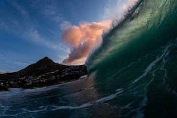huge wave crashing in the sea at sunset with lions head mountain in the background