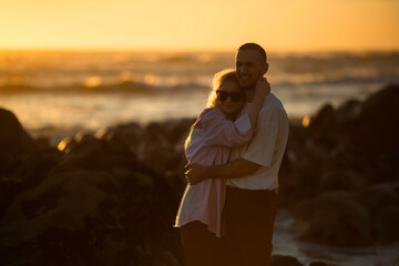 Romantic young couple embracing by the ocean during a golden sunset.