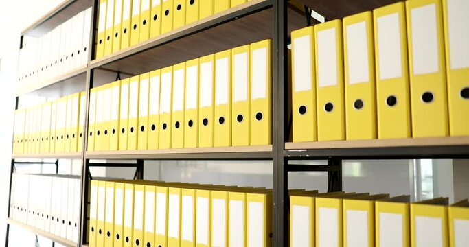 Yellow folders on a big book rack in the office, close-up. The archive has many from ring binders, slowmotion