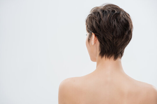 back view of young woman with short hair and bare shoulders isolated on grey.
