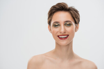 overjoyed young woman with short hair and bright makeup looking at camera isolated on grey.