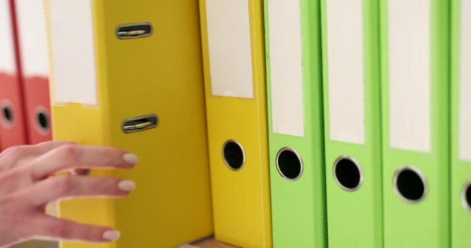 The hand takes out a yellow folder from a series of folders on the rack, a close-up. Choosing a ring binder