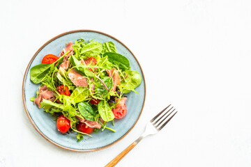 Green salad with fresh leaves, tomatoes and jamon at white table. Top view with copy space.