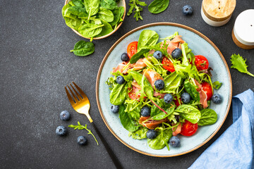 Healthy salad with prosciutto, green leaves mix and tomatoes at dark background. Top view with copy space.