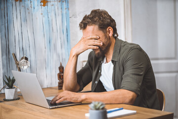 Man clearly overwhelmed and stressed out at work. His head in his hands, covering his face with...