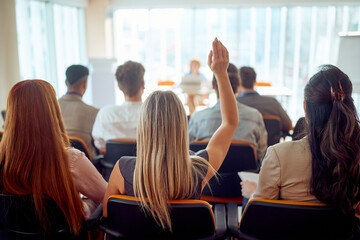 A young female participant is raising a hand to ask a question during a business lecture in the...
