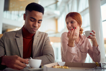 A young businessman is having a friendly talk with female colleague while they enjoying coffee after a lunch in the company building together. Business, people, company
