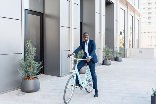 Happy black businessman riding bicycle in street