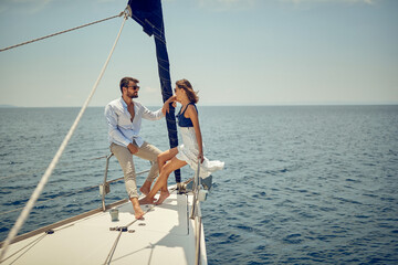 Naklejka premium A young couple is chatting on the bow of the yacht while enjoying a view and a ride on the sea. Summer, sea, vacation, relationship