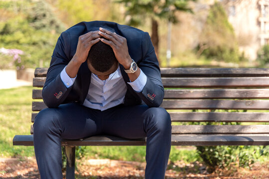 Black disappointed male entrepreneur sitting on bench in park