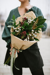 Very nice young woman holding big and beautiful bouquet of fresh tender magnolia leaves, brunia and other greenery, bouquet close up