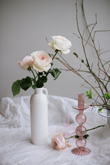 Beautiful tender pink colored English roses  in a vase, standing on the table with pink glass candle holder and some tree branches on the side - 595006461
