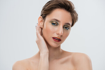 portrait of young model with bright makeup fixing shirt hair and looking at camera isolated on grey.