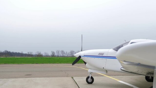 Single engine propeller airplane is standing in front of an airstrip. Transportation for tourists and locals. Small white airplane existing hangar preparing for flight. 