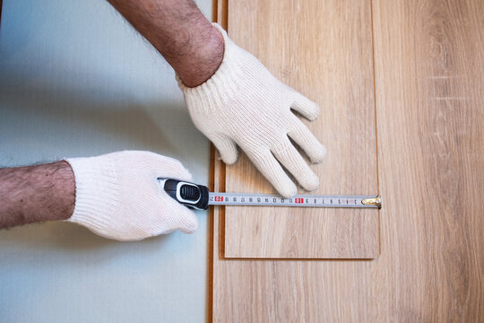 Top view of mens hands in white gloves measuring a laminate sheet with an automatic metal tape before laying flooring in a room, apartment, apartment, house, office. Carpenter at work. Builder. Worker