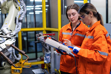 Girl engineer commissioning operating programming and looking at robot machine in the factory