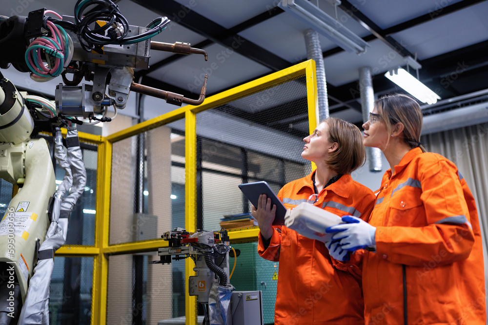 Wall mural girl engineer commissioning operating programming and looking at robot machine in the factory